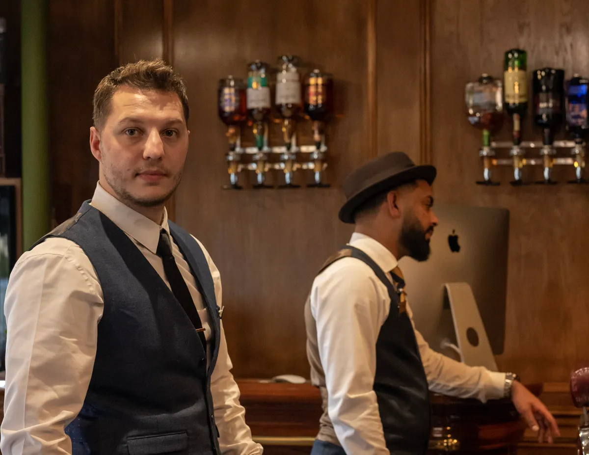 Two barbers by the spirits wall at the Boardroom